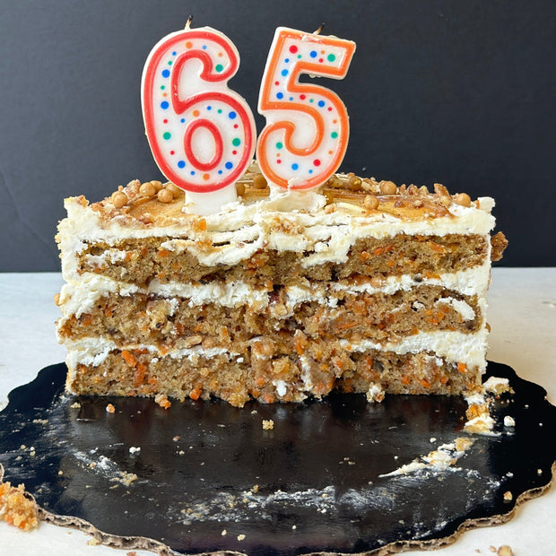 A carrot cake sliced in half with a 65 number candle on top